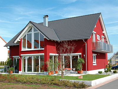 Ein rotes Einfamilienhaus mit großen Fenstern und einem Balkon, umgeben von Gartenanlagen.